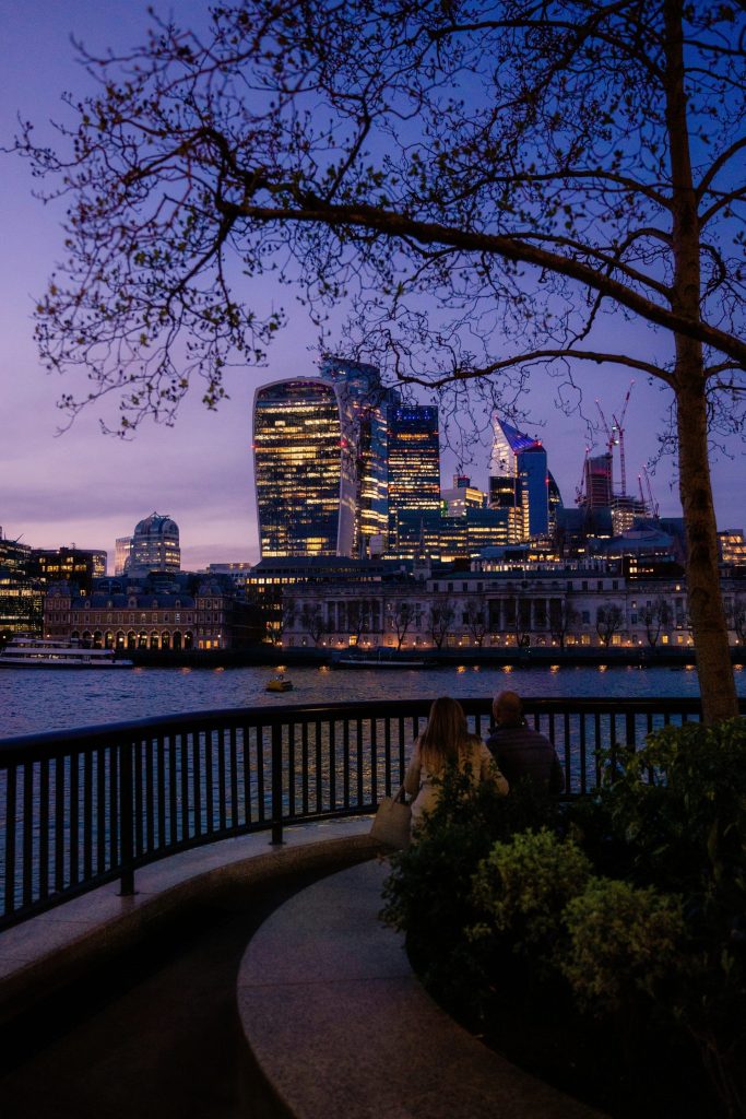 a couple sitting on a bench looking at a city at night